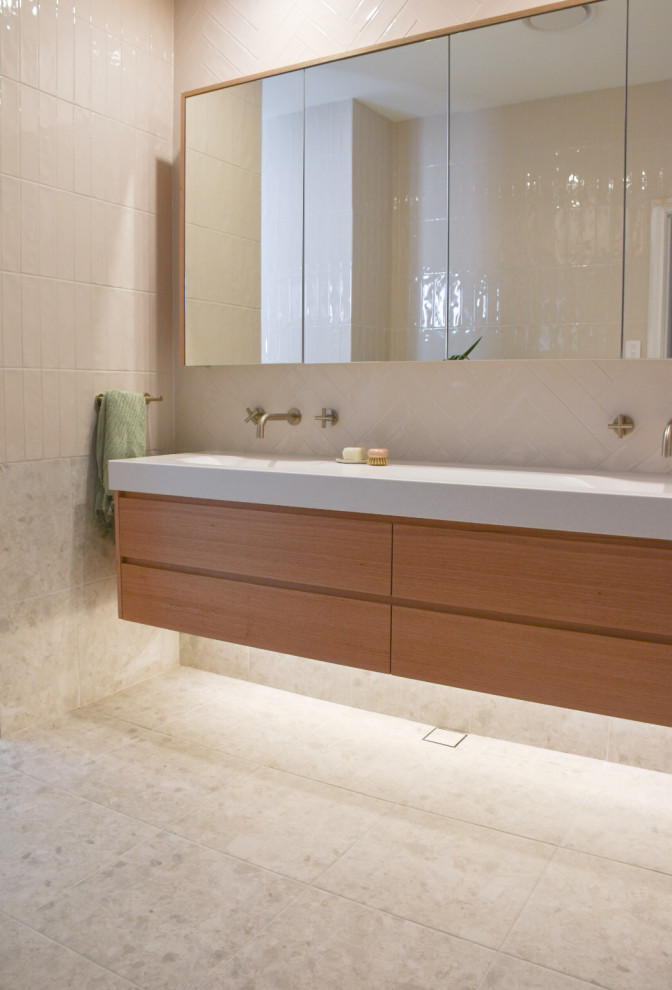 Inspiration for a medium sized contemporary bathroom in Sydney with medium wood cabinets, a freestanding bath, a walk-in shower, a wall mounted toilet, beige tiles, ceramic tiles, porcelain flooring, an integrated sink, beige floors, an open shower, white worktops, double sinks and a floating vanity unit.