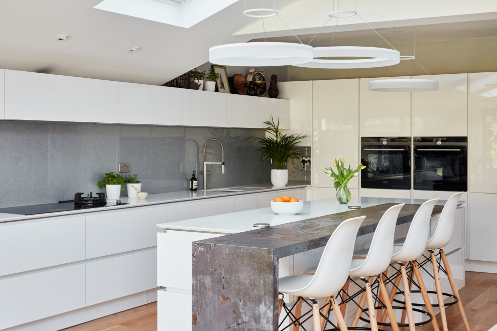 Photo of a large modern galley kitchen/diner in London with a built-in sink, flat-panel cabinets, white cabinets, granite worktops, grey splashback, metal splashback, integrated appliances, dark hardwood flooring, an island, brown floors and white worktops.