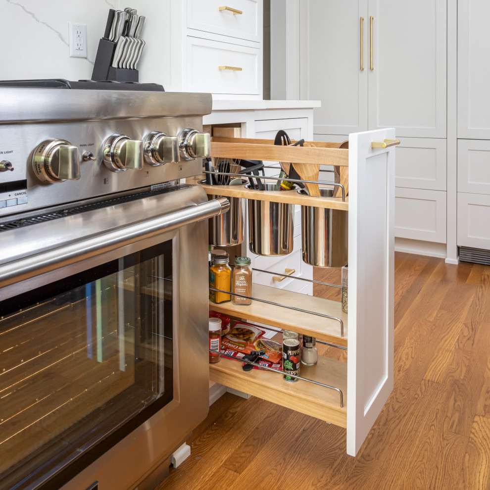 Example of a mid-sized classic single-wall medium tone wood floor, brown floor and exposed beam open concept kitchen design in Raleigh with an undermount sink, shaker cabinets, white cabinets, quartzite countertops, gray backsplash, marble backsplash, stainless steel appliances, an island and white countertops