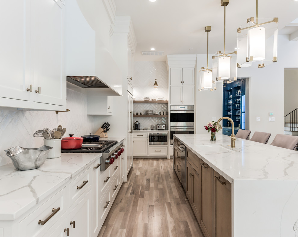 Expansive transitional l-shaped open plan kitchen in Houston with an undermount sink, shaker cabinets, light wood cabinets, quartz benchtops, white splashback, subway tile splashback, stainless steel appliances, light hardwood floors, with island, beige floor and white benchtop.