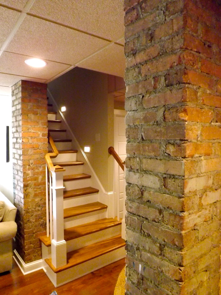 This is an example of a mid-sized traditional walk-out basement in Charlotte with beige walls, light hardwood floors, a standard fireplace and a brick fireplace surround.