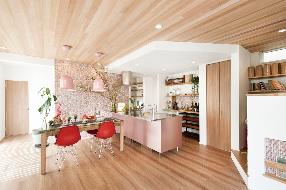 This is an example of an industrial single-wall open plan kitchen in Other with stainless steel benchtops, pink splashback, a peninsula, an integrated sink, black appliances, brown floor and medium hardwood floors.
