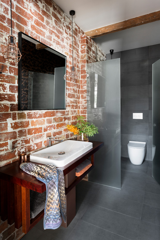 Industrial 3/4 bathroom in Melbourne with open cabinets, dark wood cabinets, a one-piece toilet, red tile, multi-coloured walls, porcelain floors, a drop-in sink, wood benchtops, grey floor and brown benchtops.
