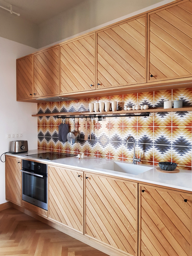This is an example of an eclectic kitchen in Other with an integrated sink, medium wood cabinets, multi-coloured splashback, mosaic tile splashback, black appliances, light hardwood floors, beige floor and flat-panel cabinets.