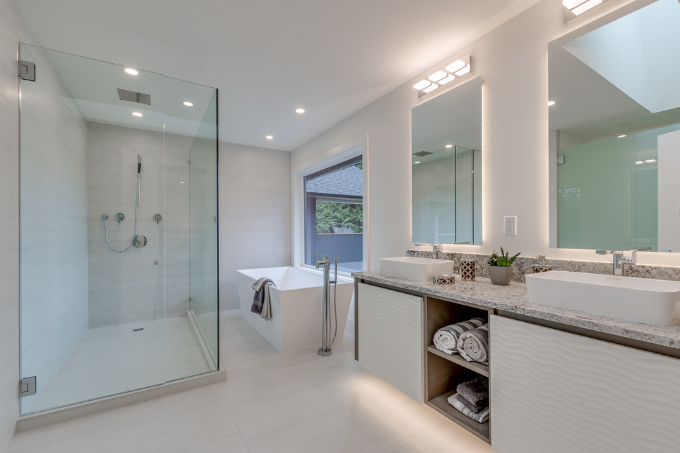 Design ideas for a modern master wet room bathroom in Vancouver with flat-panel cabinets, white cabinets, a freestanding tub, a two-piece toilet, white tile, porcelain tile, white walls, terra-cotta floors, a vessel sink, granite benchtops, white floor, a hinged shower door and multi-coloured benchtops.