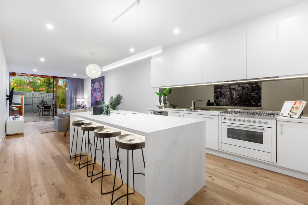This is an example of a contemporary galley kitchen in Melbourne with flat-panel cabinets, white cabinets, light hardwood floors, with island, beige floor and white benchtop.