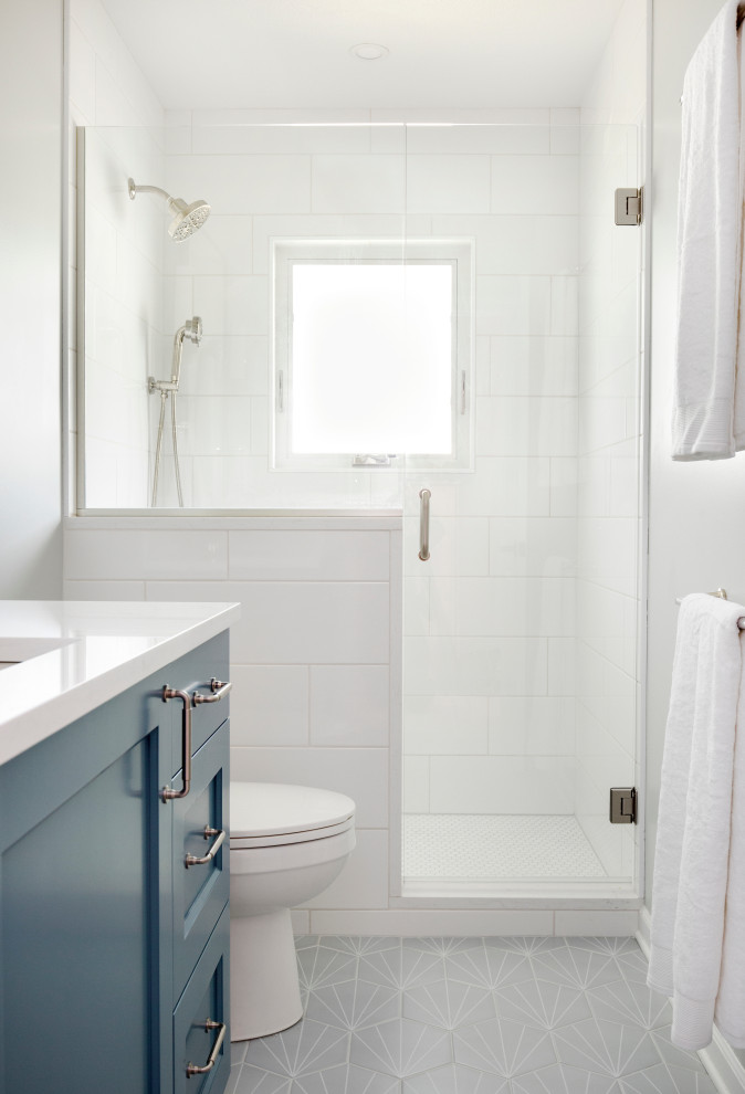 This is an example of a mid-sized transitional master bathroom in Portland with recessed-panel cabinets, blue cabinets, an alcove shower, a two-piece toilet, white tile, ceramic tile, grey walls, porcelain floors, an undermount sink, engineered quartz benchtops, grey floor, a hinged shower door, white benchtops, a niche, a single vanity and a built-in vanity.