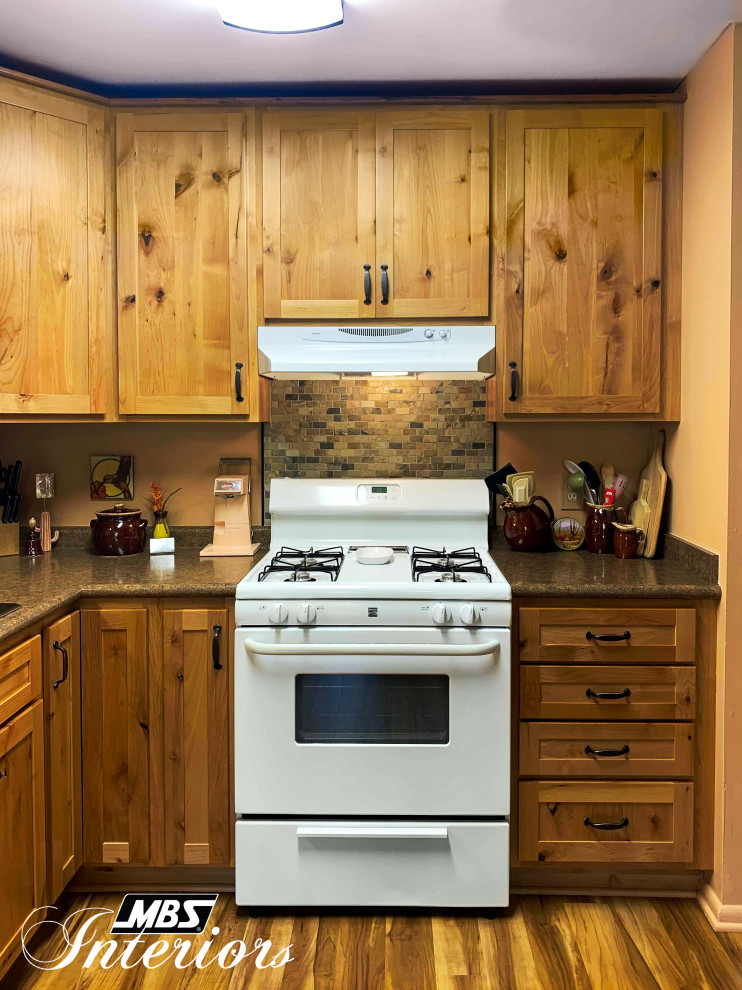 Example of a mid-sized mountain style l-shaped light wood floor and beige floor eat-in kitchen design with a drop-in sink, shaker cabinets, light wood cabinets, laminate countertops, multicolored backsplash, stone tile backsplash, white appliances, no island and brown countertops