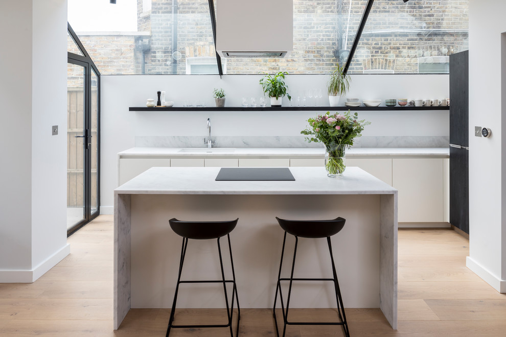 Photo of a mid-sized contemporary galley kitchen in London with an undermount sink, flat-panel cabinets, white cabinets, marble benchtops, grey splashback, marble splashback, black appliances, light hardwood floors, with island, beige floor and grey benchtop.