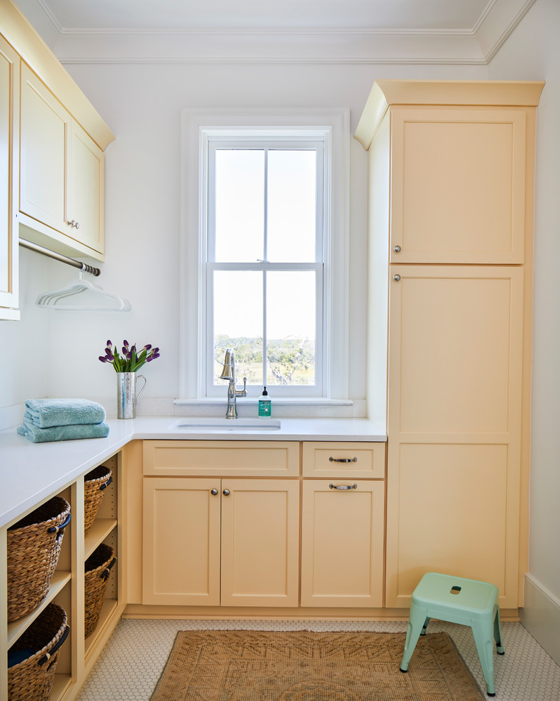 Photo of a beach style l-shaped dedicated laundry room in Charleston with an undermount sink, quartz benchtops, white walls, white floor, white benchtop, shaker cabinets and orange cabinets.