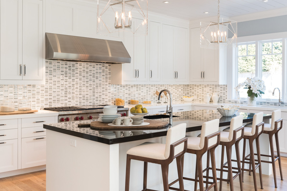 Transitional l-shaped kitchen in New York with recessed-panel cabinets, white cabinets, multi-coloured splashback, light hardwood floors, with island, black benchtop and stainless steel appliances.