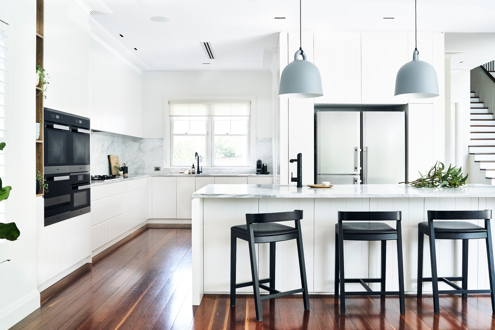 This is an example of a scandinavian l-shaped kitchen in Sydney with white cabinets, grey splashback, stone slab splashback, stainless steel appliances, medium hardwood floors, with island, brown floor and grey benchtop.