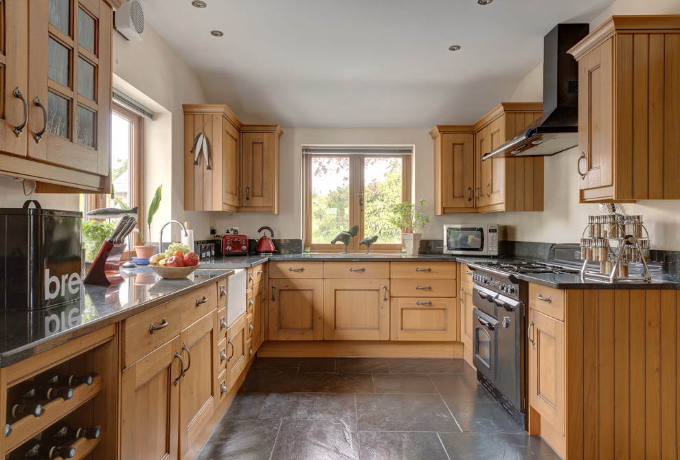 Inspiration for a mid-sized country u-shaped kitchen in Devon with recessed-panel cabinets, medium wood cabinets, granite benchtops, black appliances, a farmhouse sink, no island and grey floor.