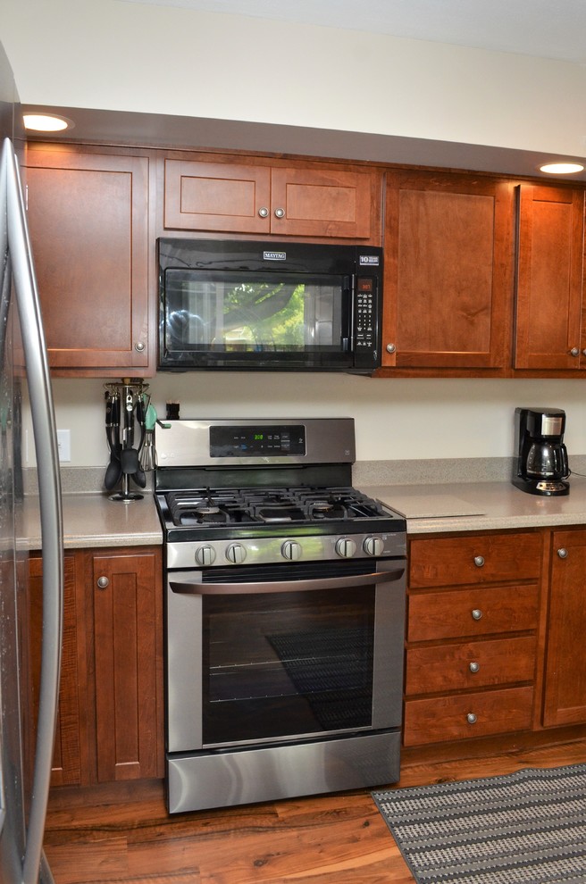 This is an example of a mid-sized transitional u-shaped eat-in kitchen in Other with a drop-in sink, shaker cabinets, dark wood cabinets, solid surface benchtops, stainless steel appliances, medium hardwood floors, a peninsula, brown floor and grey benchtop.