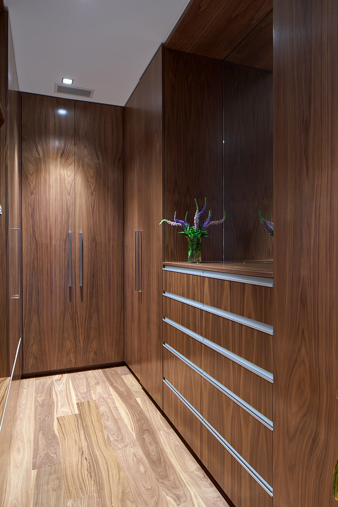 Contemporary gender-neutral walk-in wardrobe in New York with flat-panel cabinets, dark wood cabinets, light hardwood floors and beige floor.