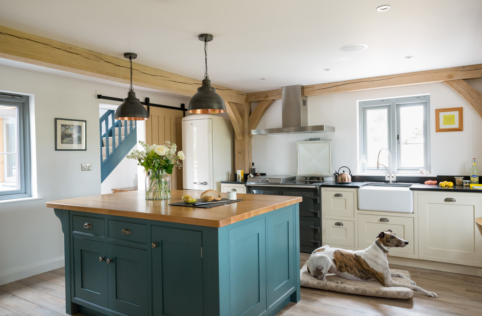 Inspiration for a country separate kitchen in West Midlands with a farmhouse sink, shaker cabinets, beige cabinets, black appliances, light hardwood floors, with island and black benchtop.