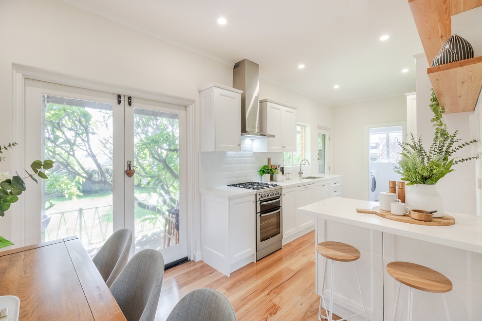 Mid-sized contemporary galley eat-in kitchen in Adelaide with an undermount sink, shaker cabinets, white cabinets, quartz benchtops, white splashback, subway tile splashback, stainless steel appliances, light hardwood floors, with island, yellow floor and white benchtop.