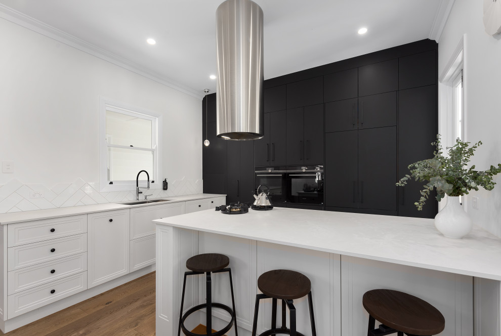 This is an example of a mid-sized traditional l-shaped eat-in kitchen in Brisbane with an undermount sink, shaker cabinets, white cabinets, quartz benchtops, white splashback, subway tile splashback, black appliances, laminate floors, with island, brown floor and white benchtop.