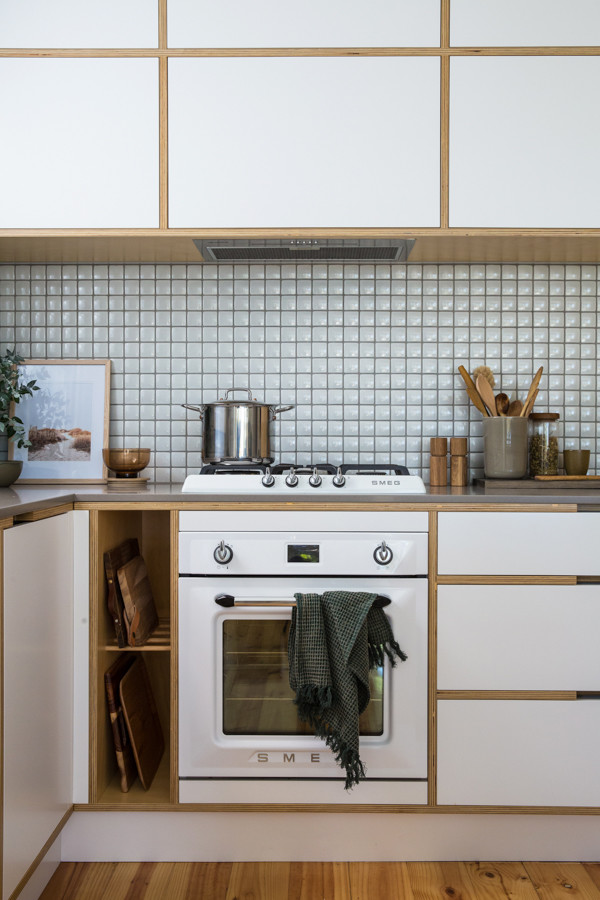 Photo of a small scandinavian l-shaped eat-in kitchen in Adelaide with an undermount sink, flat-panel cabinets, white cabinets, solid surface benchtops, grey splashback, ceramic splashback, white appliances, medium hardwood floors, with island, brown floor and grey benchtop.