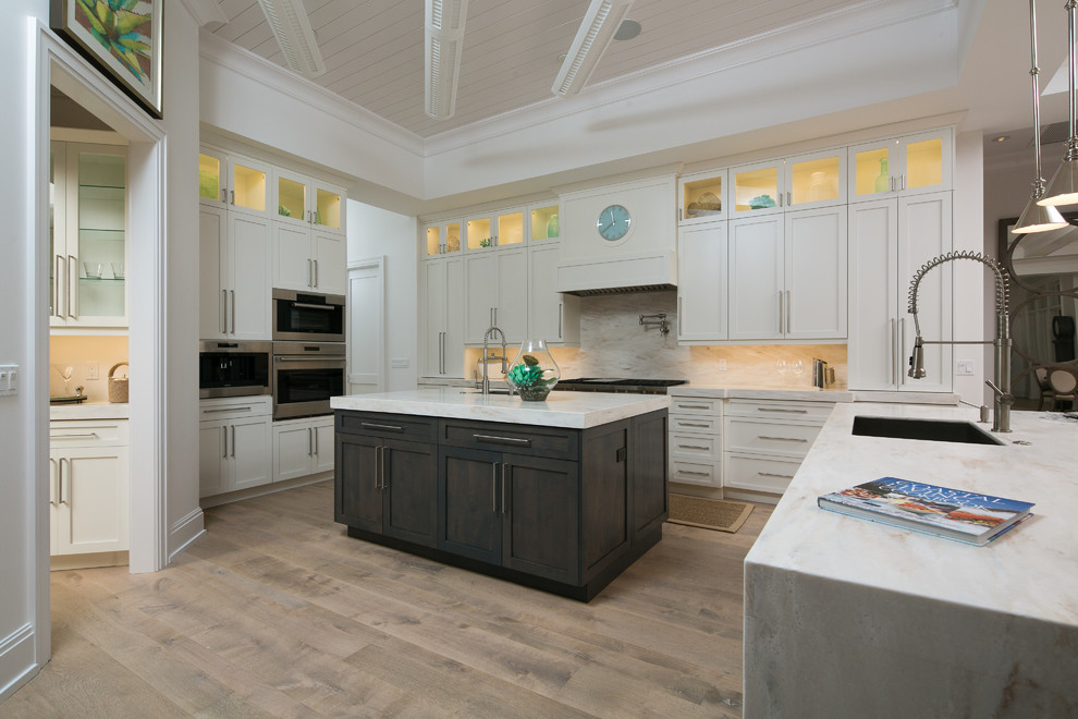 Example of a large transitional u-shaped light wood floor eat-in kitchen design in Miami with an undermount sink, shaker cabinets, white cabinets, marble countertops, white backsplash, stone slab backsplash, stainless steel appliances and an island
