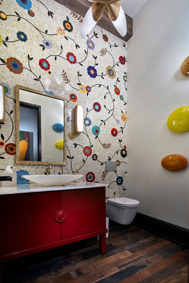 Photo of a large transitional powder room in Dallas with flat-panel cabinets, red cabinets, a wall-mount toilet, multi-coloured tile, glass tile, multi-coloured walls, medium hardwood floors, a vessel sink, brown floor, white benchtops and onyx benchtops.