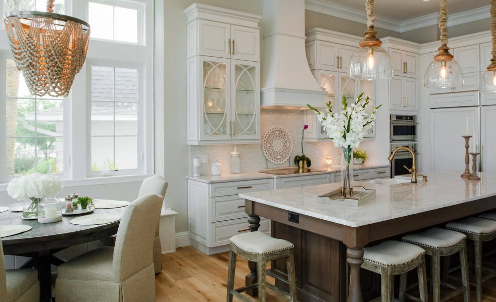 Inspiration for a coastal l-shaped medium tone wood floor and brown floor kitchen remodel in Tampa with an integrated sink, raised-panel cabinets, white cabinets, white backsplash, mosaic tile backsplash, paneled appliances, an island and white countertops