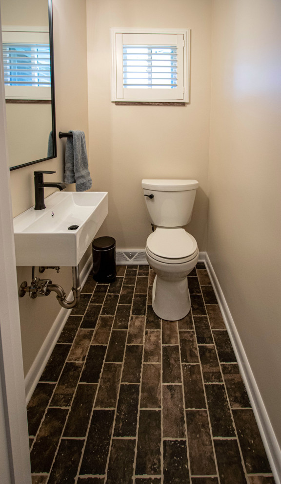 Foto på ett litet toalett, med en toalettstol med separat cisternkåpa, beige väggar, klinkergolv i keramik, ett väggmonterat handfat och brunt golv