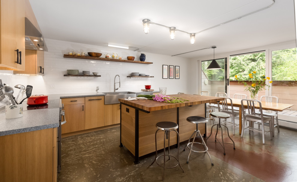 This is an example of a midcentury l-shaped eat-in kitchen in Burlington with a farmhouse sink, flat-panel cabinets, light wood cabinets, white splashback, with island, multi-coloured floor and grey benchtop.