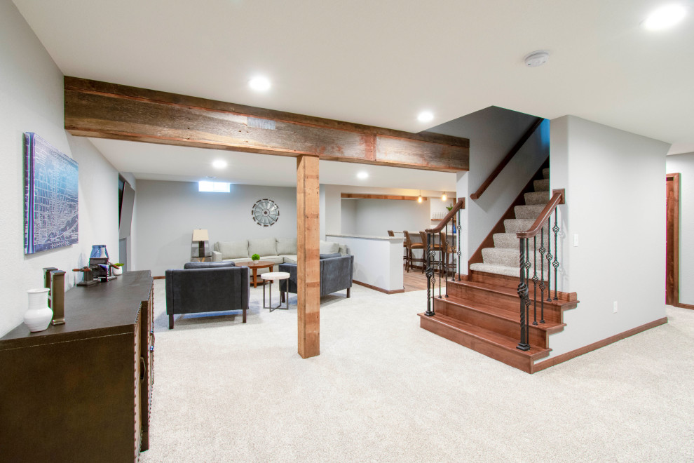 Photo of an expansive transitional fully buried basement in Milwaukee with a home bar, grey walls, carpet, beige floor, exposed beam and wood walls.