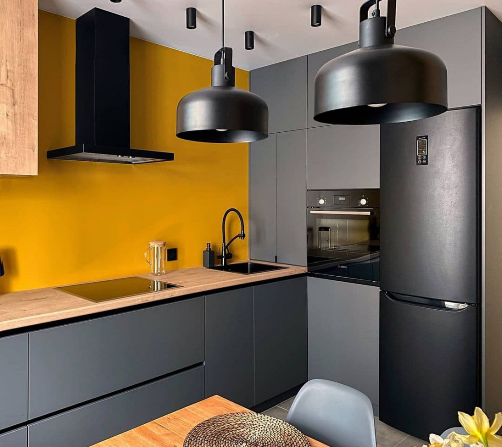 Inspiration for a mid-sized contemporary l-shaped eat-in kitchen in Moscow with an undermount sink, flat-panel cabinets, grey cabinets, wood benchtops, orange splashback, limestone splashback, black appliances, ceramic floors, no island, grey floor and brown benchtop.