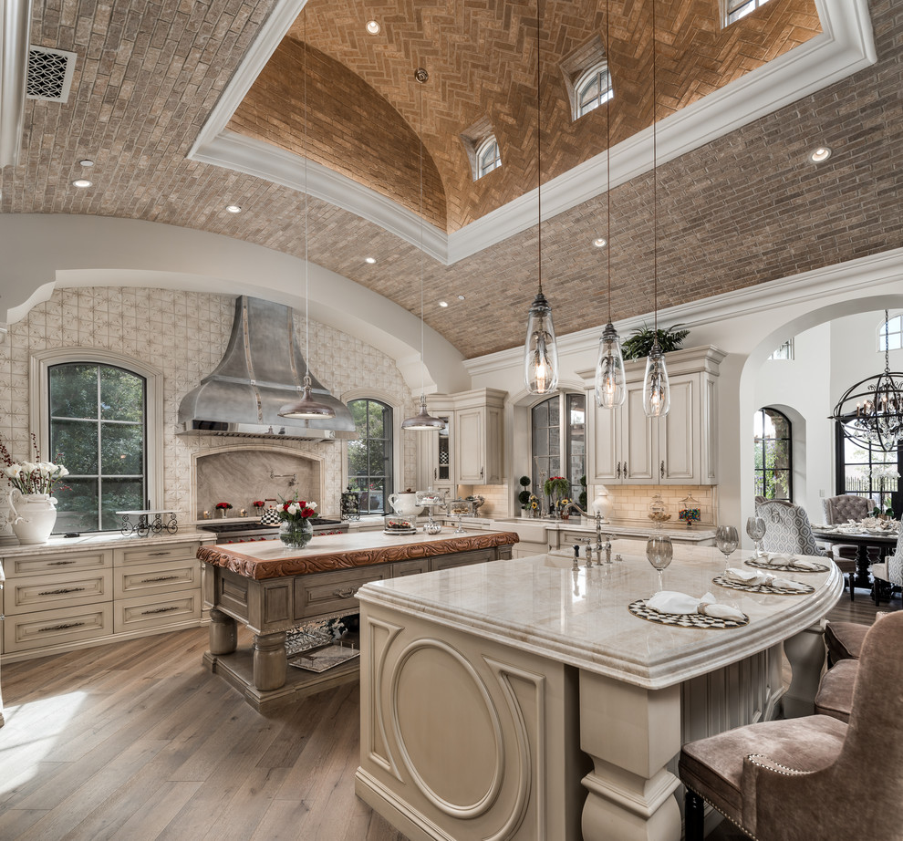 Enclosed kitchen - huge transitional u-shaped brown floor, dark wood floor and vaulted ceiling enclosed kitchen idea in Phoenix with a farmhouse sink, raised-panel cabinets, light wood cabinets, quartzite countertops, white backsplash, paneled appliances, two islands, porcelain backsplash and beige countertops