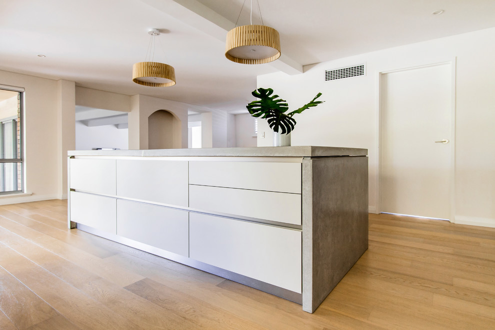 Mid-sized contemporary eat-in kitchen in Perth with flat-panel cabinets, white cabinets, concrete benchtops, stainless steel appliances, light hardwood floors, with island and a drop-in sink.