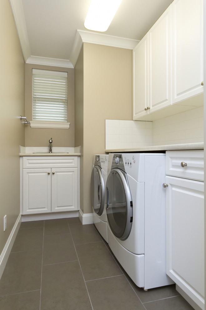 Inspiration for a mid-sized traditional single-wall utility room in Richmond with a drop-in sink, raised-panel cabinets, a side-by-side washer and dryer, medium wood cabinets, solid surface benchtops, grey walls and light hardwood floors.
