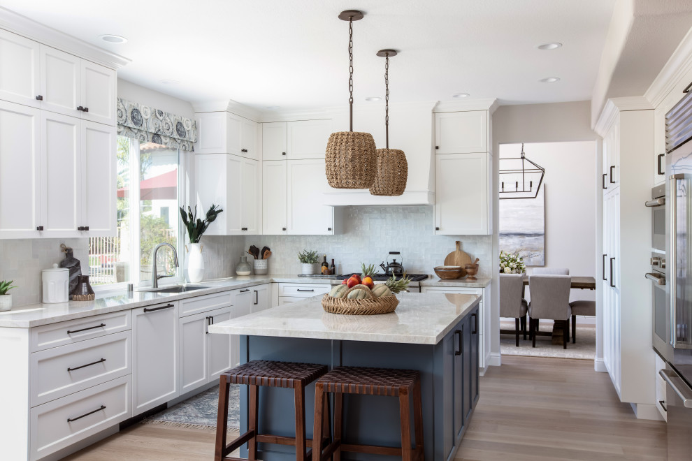 This is an example of a large beach style u-shaped open plan kitchen in Denver with a submerged sink, recessed-panel cabinets, blue cabinets, quartz worktops, white splashback, ceramic splashback, stainless steel appliances, medium hardwood flooring, an island, brown floors and white worktops.