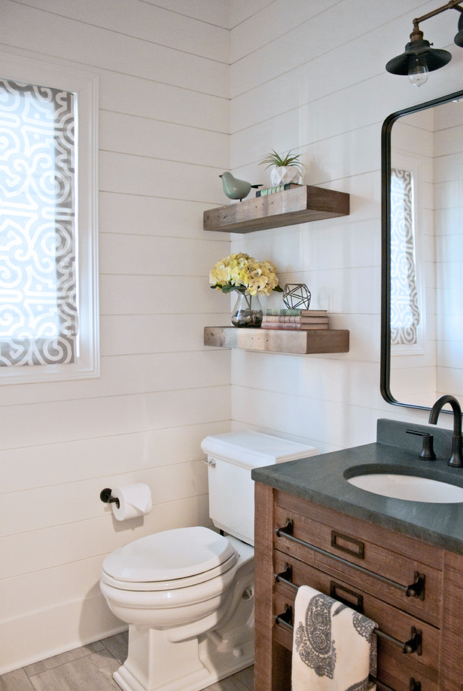 Small industrial powder room with distressed cabinets, a two-piece toilet, ceramic floors, an undermount sink, soapstone benchtops, grey floor and white walls.