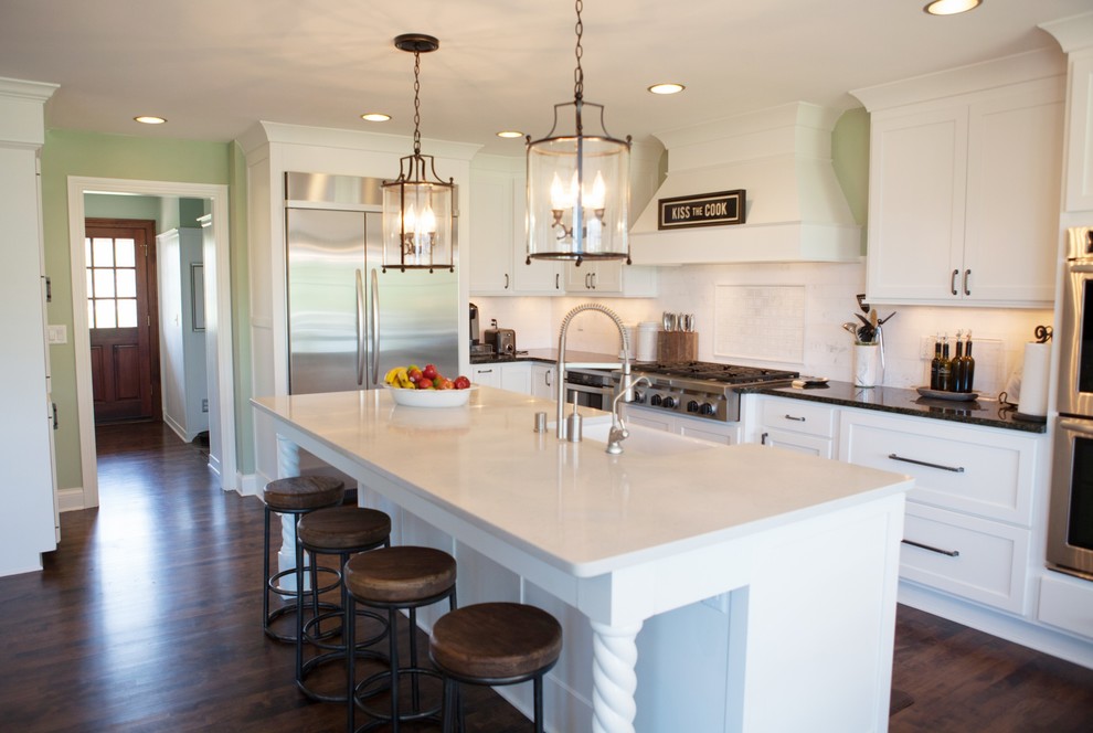 Photo of a traditional l-shaped kitchen in Milwaukee with a farmhouse sink, shaker cabinets, white cabinets, white splashback and stainless steel appliances.