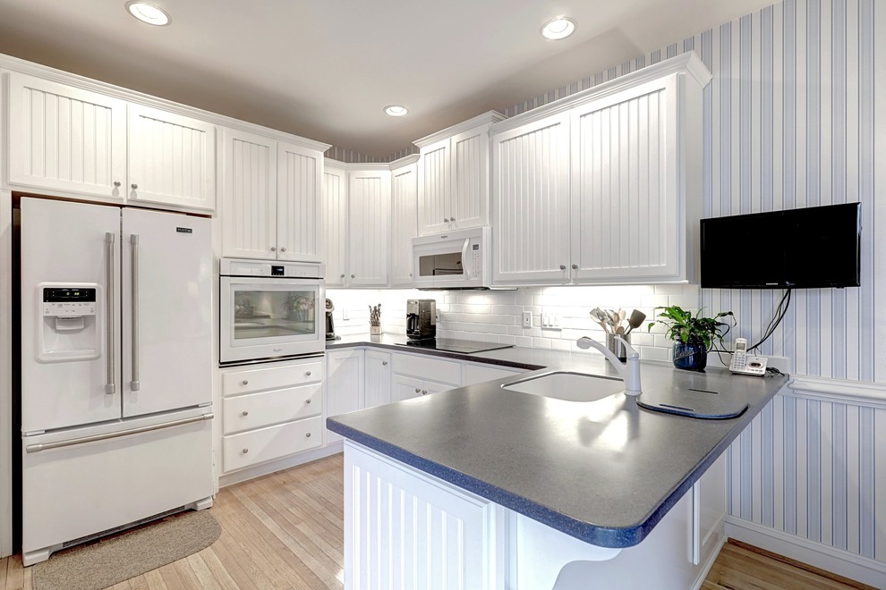 Mid-sized beach style u-shaped kitchen pantry in Other with a single-bowl sink, white cabinets, quartz benchtops, white splashback, subway tile splashback, stainless steel appliances, plywood floors, a peninsula, beige floor and raised-panel cabinets.