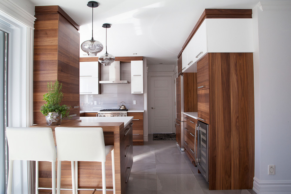 Photo of a contemporary u-shaped kitchen in Montreal with flat-panel cabinets, medium wood cabinets, grey splashback, stainless steel appliances and a peninsula.
