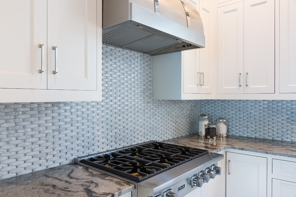 Example of a large transitional l-shaped medium tone wood floor eat-in kitchen design with a farmhouse sink, recessed-panel cabinets, white cabinets, marble countertops, gray backsplash, porcelain backsplash, stainless steel appliances and an island