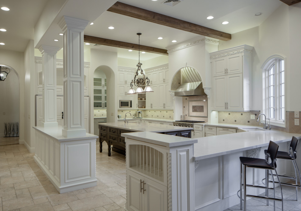 Design ideas for an expansive transitional u-shaped open plan kitchen in Orange County with a double-bowl sink, raised-panel cabinets, white cabinets, quartz benchtops, beige splashback, limestone splashback, stainless steel appliances, limestone floors, with island, beige floor and beige benchtop.
