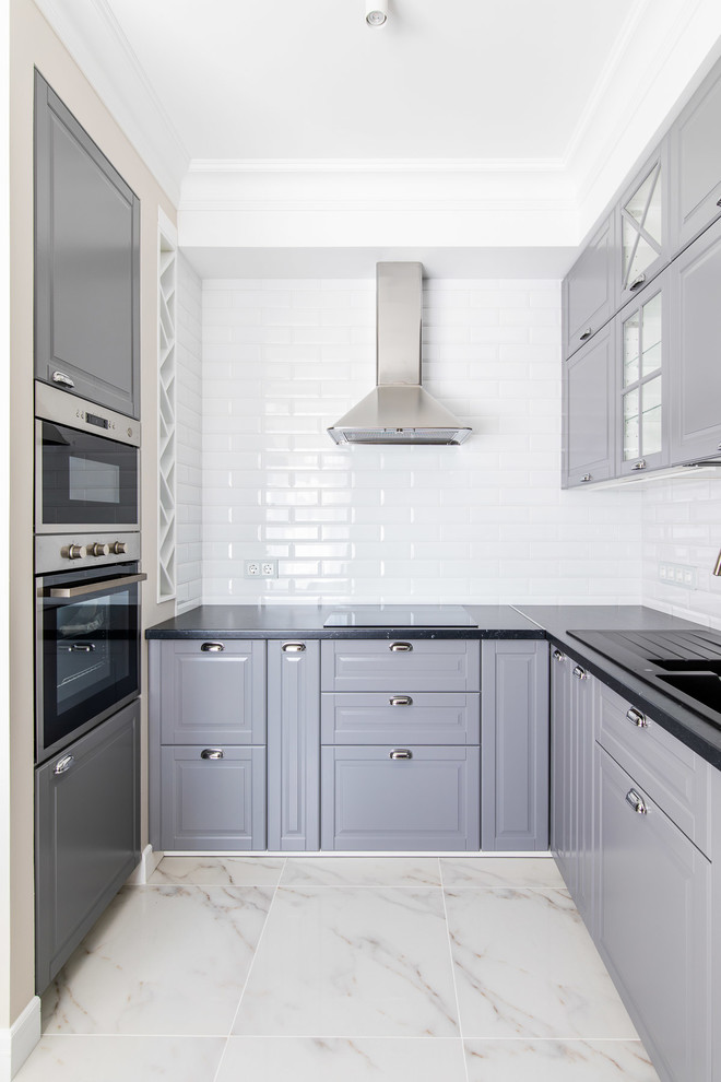 Contemporary u-shaped kitchen in Saint Petersburg with a double-bowl sink, raised-panel cabinets, grey cabinets, white splashback, subway tile splashback, white floor and black benchtop.