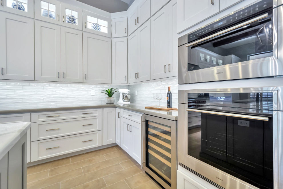 Large transitional l-shaped porcelain tile and brown floor eat-in kitchen photo in Phoenix with a farmhouse sink, shaker cabinets, white cabinets, quartz countertops, white backsplash, subway tile backsplash, stainless steel appliances, an island and gray countertops