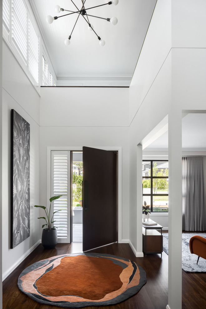 This is an example of a large contemporary foyer in Sydney with white walls, dark hardwood floors, a single front door and a dark wood front door.