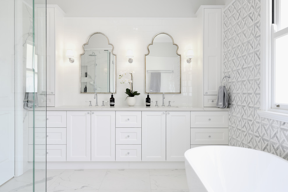 Design ideas for a mid-sized beach style master bathroom in Gold Coast - Tweed with white cabinets, gray tile, white walls, a hinged shower door, an enclosed toilet, a double vanity, a built-in vanity, recessed-panel cabinets, a drop-in tub, an alcove shower, ceramic tile, ceramic floors, a drop-in sink, engineered quartz benchtops, white floor and white benchtops.