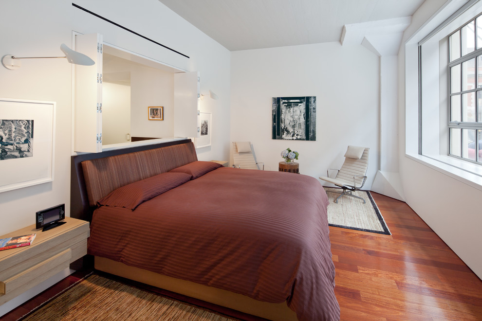 This is an example of a contemporary master bedroom in New York with white walls and medium hardwood floors.