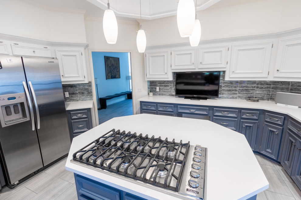 Example of a mid-sized transitional u-shaped ceramic tile and gray floor enclosed kitchen design in Austin with a farmhouse sink, recessed-panel cabinets, white cabinets, quartzite countertops, blue backsplash, glass tile backsplash, stainless steel appliances, an island and white countertops