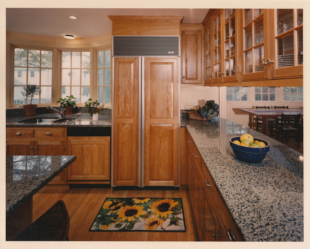 Photo of a mid-sized traditional l-shaped open plan kitchen in Boston with raised-panel cabinets, medium wood cabinets, granite benchtops, with island, a double-bowl sink, light hardwood floors and panelled appliances.