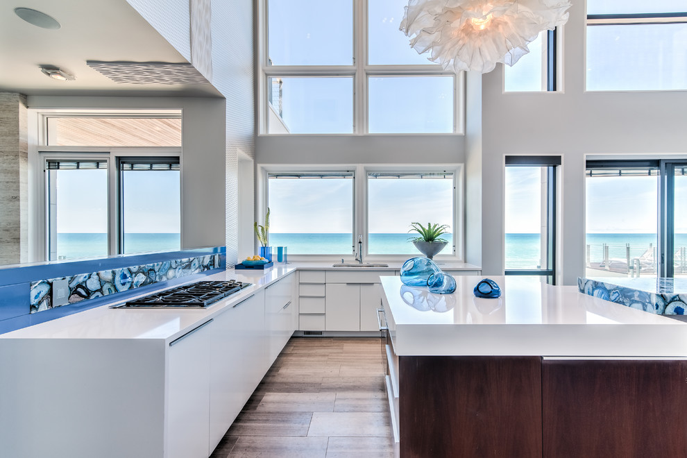 Design ideas for an expansive modern l-shaped open plan kitchen in Chicago with an undermount sink, flat-panel cabinets, white cabinets, quartzite benchtops, blue splashback, stone slab splashback, panelled appliances, limestone floors, multiple islands and brown floor.
