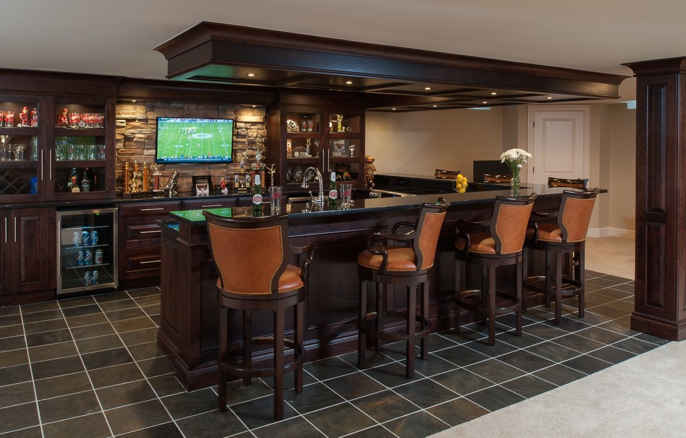 Inspiration for a large transitional galley seated home bar in Detroit with raised-panel cabinets, dark wood cabinets, granite benchtops, beige splashback, stone tile splashback, an undermount sink and slate floors.