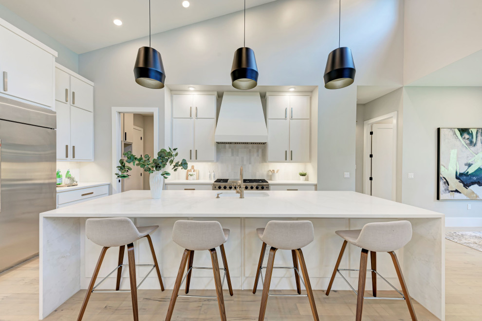 Design ideas for a contemporary l-shaped kitchen in Austin with an undermount sink, flat-panel cabinets, white cabinets, white splashback, stainless steel appliances, light hardwood floors, with island, beige floor, white benchtop and vaulted.